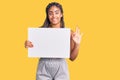 Young african american woman with braids holding blank empty banner doing ok sign with fingers, smiling friendly gesturing Royalty Free Stock Photo