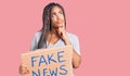 Young african american woman with braids holding fake news banner serious face thinking about question with hand on chin,