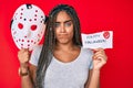 Young african american woman with braids holding halloween banner and scary mask skeptic and nervous, frowning upset because of