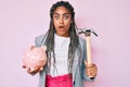 Young african american woman with braids holding piggy bank and hammer afraid and shocked with surprise and amazed expression, Royalty Free Stock Photo