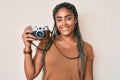 Young african american woman with braids holding vintage camera looking positive and happy standing and smiling with a confident Royalty Free Stock Photo