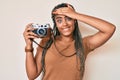 Young african american woman with braids holding vintage camera stressed and frustrated with hand on head, surprised and angry Royalty Free Stock Photo