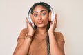 Young african american woman with braids listening to music using headphones looking at the camera blowing a kiss being lovely and Royalty Free Stock Photo