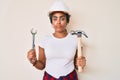 Young african american woman with braids wearing hardhat holding hammer and wrench relaxed with serious expression on face Royalty Free Stock Photo