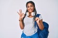 Young african american woman with braids wearing student backpack and headphones doing ok sign with fingers, smiling friendly Royalty Free Stock Photo