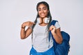 Young african american woman with braids wearing student backpack and headphones pointing finger to one self smiling happy and Royalty Free Stock Photo