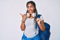 Young african american woman with braids wearing student backpack and headphones pointing thumb up to the side smiling happy with Royalty Free Stock Photo