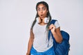 Young african american woman with braids wearing student backpack and headphones scared and amazed with open mouth for surprise, Royalty Free Stock Photo