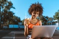 young african-american woman in bright sports bra sitting at sport court with laptop