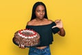 Young african american woman celebrating birthday holding big chocolate cake with angry face, negative sign showing dislike with Royalty Free Stock Photo