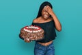 Young african american woman celebrating birthday holding big chocolate cake stressed and frustrated with hand on head, surprised Royalty Free Stock Photo