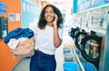 Young african american woman with curly hair smiling happy doing chores at the laundry speaking on the phone Royalty Free Stock Photo