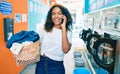 Young african american woman with curly hair smiling happy doing chores at the laundry speaking on the phone Royalty Free Stock Photo