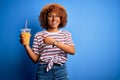 Young African American woman with curly hair on vacation wearing hat drinking orange juice very happy pointing with hand and Royalty Free Stock Photo