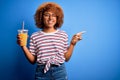 Young African American woman with curly hair on vacation wearing hat drinking orange juice very happy pointing with hand and Royalty Free Stock Photo