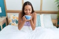 Young african american woman drinking cup of coffee sitting on bed at bedroom Royalty Free Stock Photo