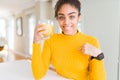 Young african american woman drinking a glass of fresh orange juice with surprise face pointing finger to himself Royalty Free Stock Photo