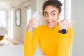 Young african american woman drinking a glass of fresh water pointing and showing with thumb up to the side with happy face Royalty Free Stock Photo