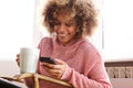Young African American Woman Drinking Hot Cup Of Coffee And Looking At Cellphone