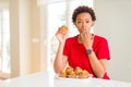 Young african american woman eating chocolate chips muffins cover mouth with hand shocked with shame for mistake, expression of Royalty Free Stock Photo