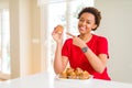 Young african american woman eating chocolate chips muffins very happy pointing with hand and finger