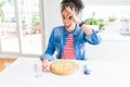 Young african american woman eating homemade cheese pizza with happy face smiling doing ok sign with hand on eye looking through Royalty Free Stock Photo