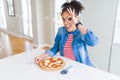 Young african american woman eating homemade mozzarella cheese pizza with happy face smiling doing ok sign with hand on eye Royalty Free Stock Photo