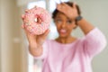 Young african american woman eating pink sugar donut stressed with hand on head, shocked with shame and surprise face, angry and Royalty Free Stock Photo