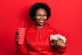 Young african american woman eating popcorn and drinking soda winking looking at the camera with sexy expression, cheerful and Royalty Free Stock Photo