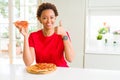Young african american woman eating tasty peperoni pizza happy with big smile doing ok sign, thumb up with fingers, excellent sign Royalty Free Stock Photo