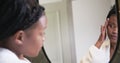 Young African American woman examines her face in a mirror at home