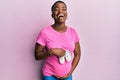 Young african american woman expecting a baby holding shoes smiling and laughing hard out loud because funny crazy joke Royalty Free Stock Photo