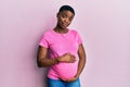 Young african american woman expecting a baby, touching pregnant belly relaxed with serious expression on face Royalty Free Stock Photo