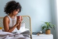 Young African American woman having morning coffee in bed. Multiracial latina female relaxing in bedroom having tea. Royalty Free Stock Photo