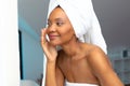 Young african american woman with head wrapped in white towel touching her cheek in bathroom Royalty Free Stock Photo