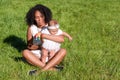 Young african american woman and her daughter sitting on green grass in summer park. Black mother playing with her baby girl Royalty Free Stock Photo