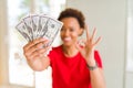 Young african american woman holding bank notes of fifty dollars doing ok sign with fingers, excellent symbol