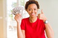 Young african american woman holding bank notes of fifty dollars happy with big smile doing ok sign, thumb up with fingers,