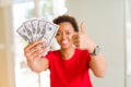 Young african american woman holding bank notes of fifty dollars happy with big smile doing ok sign, thumb up with fingers,