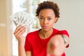 Young african american woman holding bank notes of twenty dollars pointing with finger to the camera and to you, hand sign, Royalty Free Stock Photo