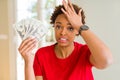 Young african american woman holding bank notes of twenty dollars stressed with hand on head, shocked with shame and surprise Royalty Free Stock Photo