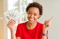 Young african american woman holding bank notes of twenty dollars very happy pointing with hand and finger to the side Royalty Free Stock Photo