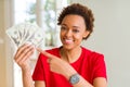 Young african american woman holding bank notes of twenty dollars very happy pointing with hand and finger Royalty Free Stock Photo