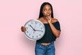 Young african american woman holding big clock serious face thinking about question with hand on chin, thoughtful about confusing Royalty Free Stock Photo