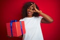 Young african american woman holding birthday gift standing over isolated red background with happy face smiling doing ok sign Royalty Free Stock Photo