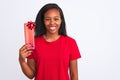 Young african american woman holding birthday present over isolated background with a happy face standing and smiling with a Royalty Free Stock Photo