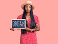 Young african american woman holding blackboard with dream word thinking attitude and sober expression looking self confident