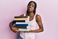 Young african american woman holding books clueless and confused expression Royalty Free Stock Photo