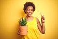 Young african american woman holding cactus pot over isolated yellow background surprised with an idea or question pointing finger Royalty Free Stock Photo