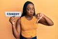 Young african american woman holding comedy word paper with angry face, negative sign showing dislike with thumbs down, rejection